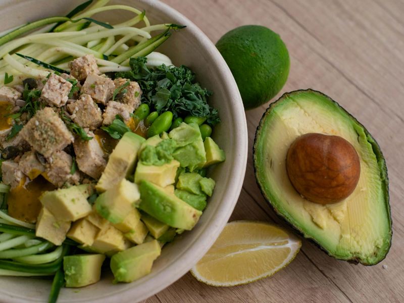 delicious vegan bowl with zoodles, avocado, tofu, and greens on a wood image